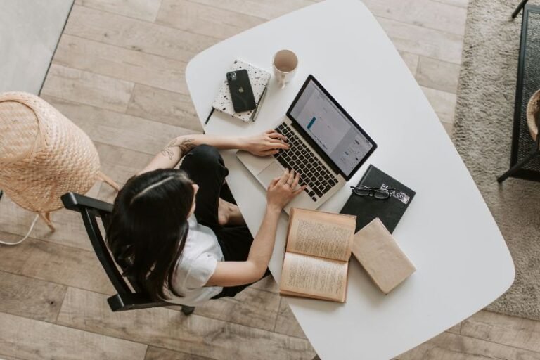 Mulher em uma mesa de café com laptop, xícara de café, smartphone com Instagram aberto e bloco de notas.